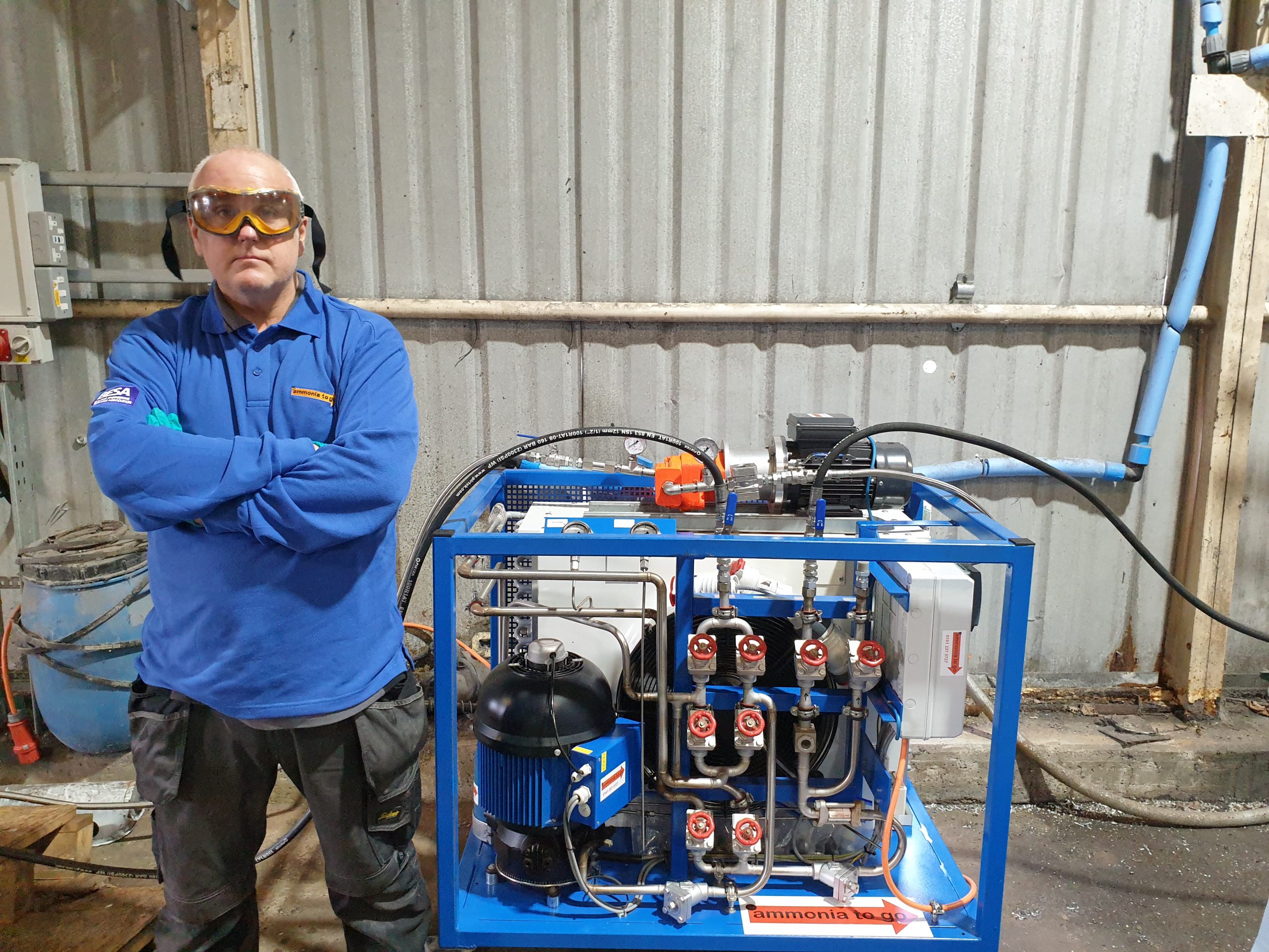 An engineer wearing a blue ammonia to go refrigerant recovery shirt next to a pump out unit